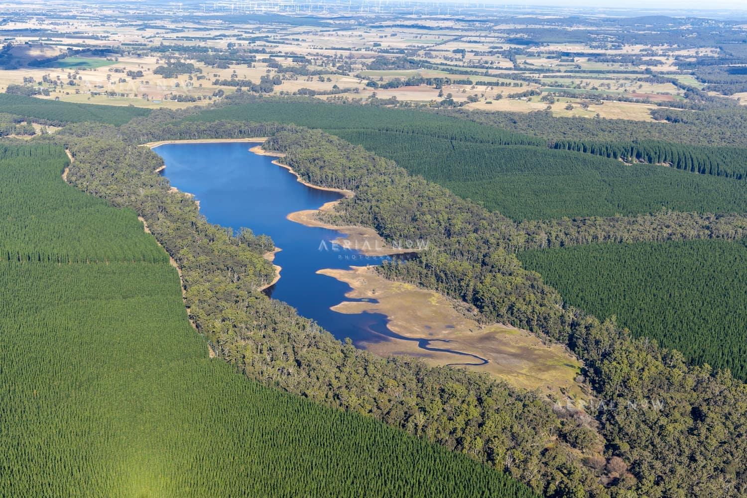 Aerial view of a long inlet of Bostock Reservoir at Spargo Creek, with exposed shoreline, native bushland, pine plantation forest and rural farmland beyond.