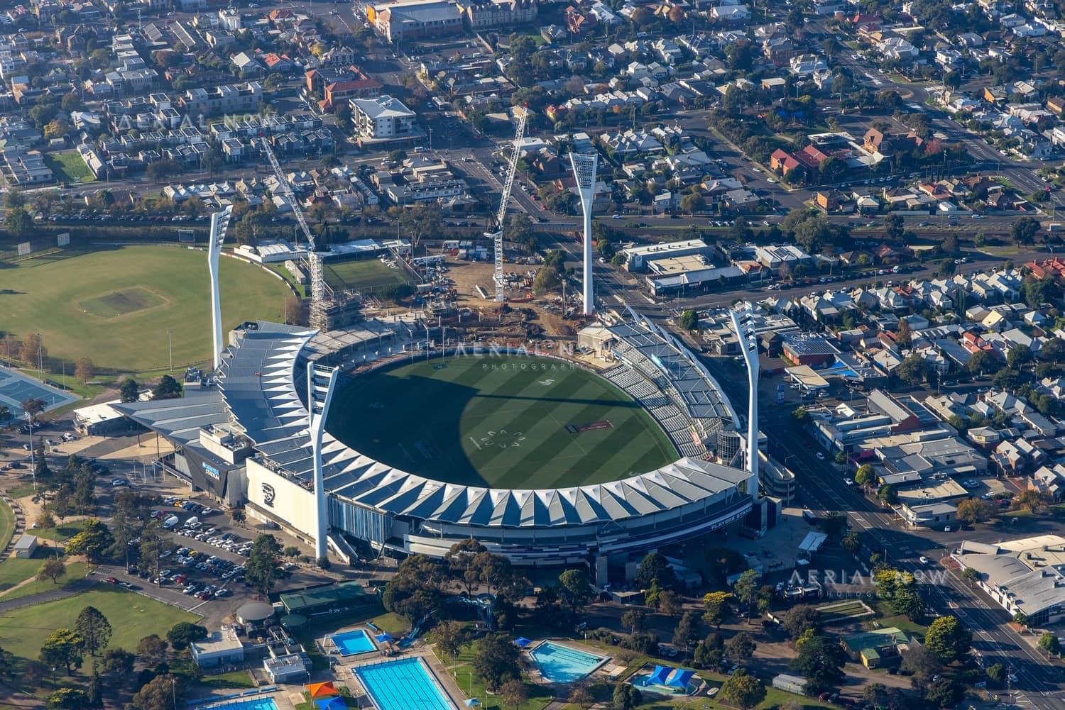 Aerial view of GMHBA Stadium at Kardinia Park in South Geelong, showing the oval, grandstands, light towers, surrounding streets and nearby parkland.