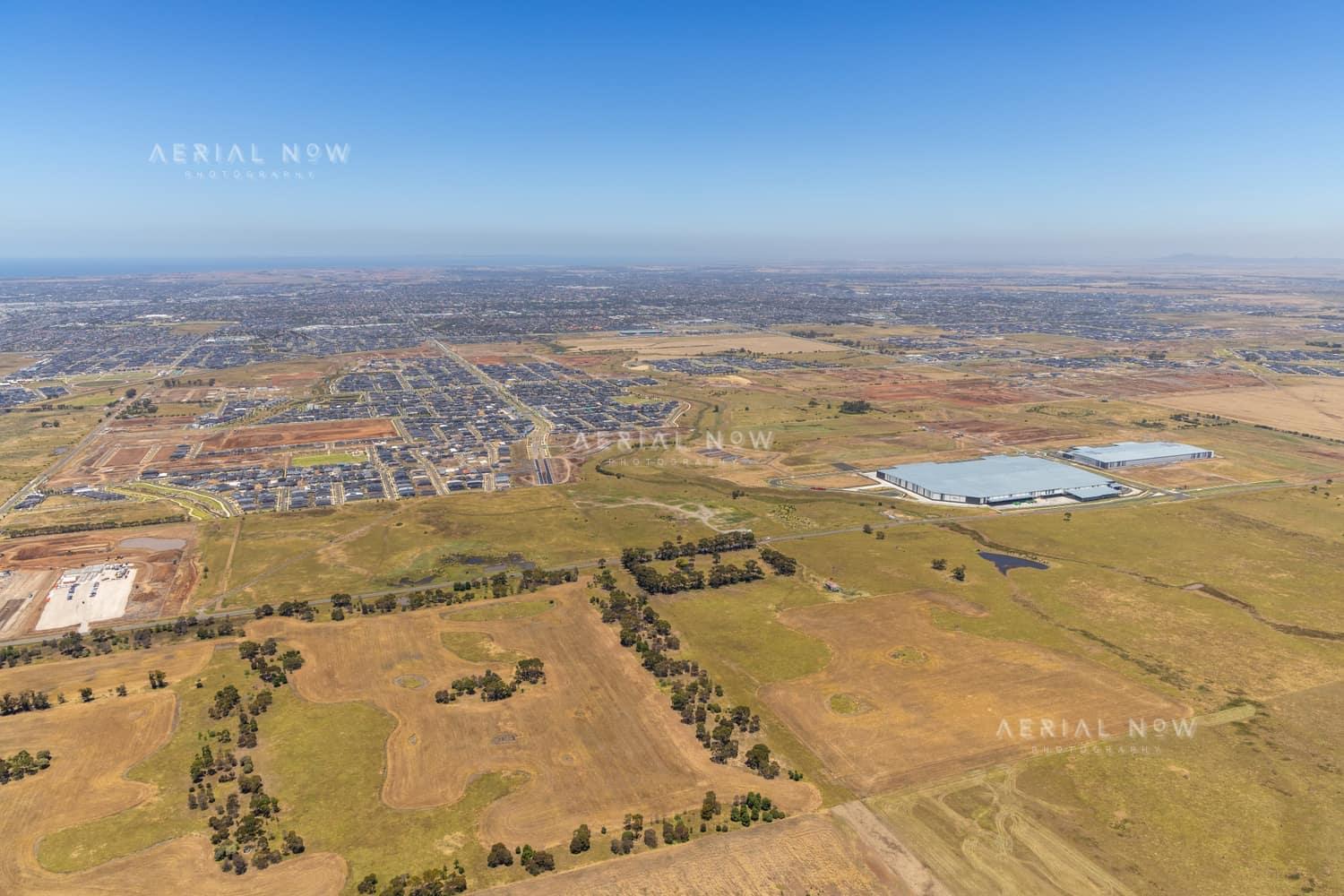 Wide aerial view over Boundary Road in Truganina, showing established warehouses, expanding housing estates, open farmland and the future Djeembana logistics precinct in Melbourne's west.