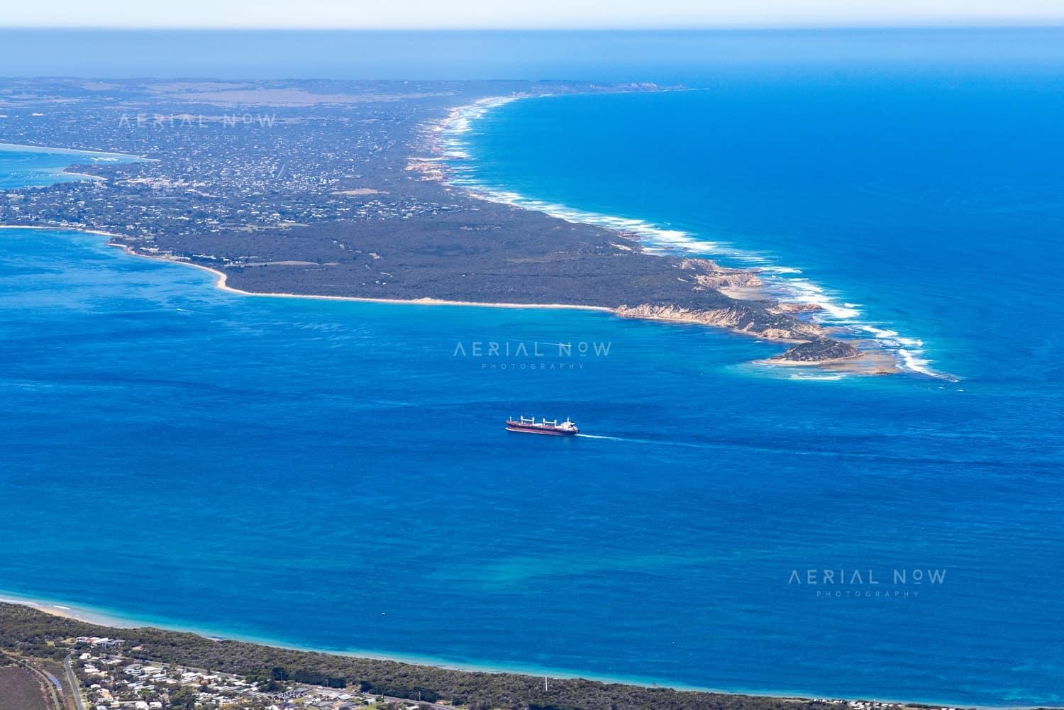Aerial view of Port Phillip Heads and Point Nepean from Point Lonsdale, with a cargo ship crossing blue water between the coastline and surf beaches.