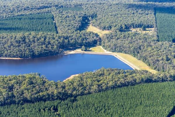 Aerial view of Bostock Reservoir at Bolwarrah, showing the dam wall, blue water storage, surrounding forest and pine plantation.