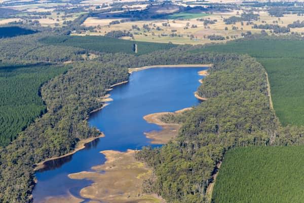 Aerial view of Bostock Reservoir near Spargo Creek, showing shallow inlet wetlands, surrounding bushland, plantation forest and rural farmland beyond.