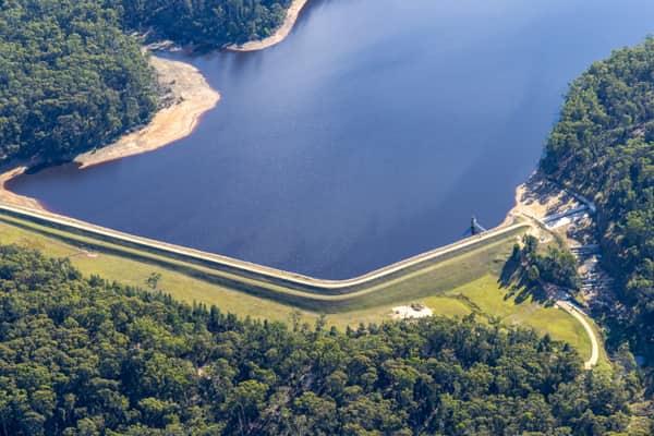 Aerial view of Bostock Reservoir at Spargo Creek VIC, showing the curved dam wall, outlet area, dark water and surrounding forest.