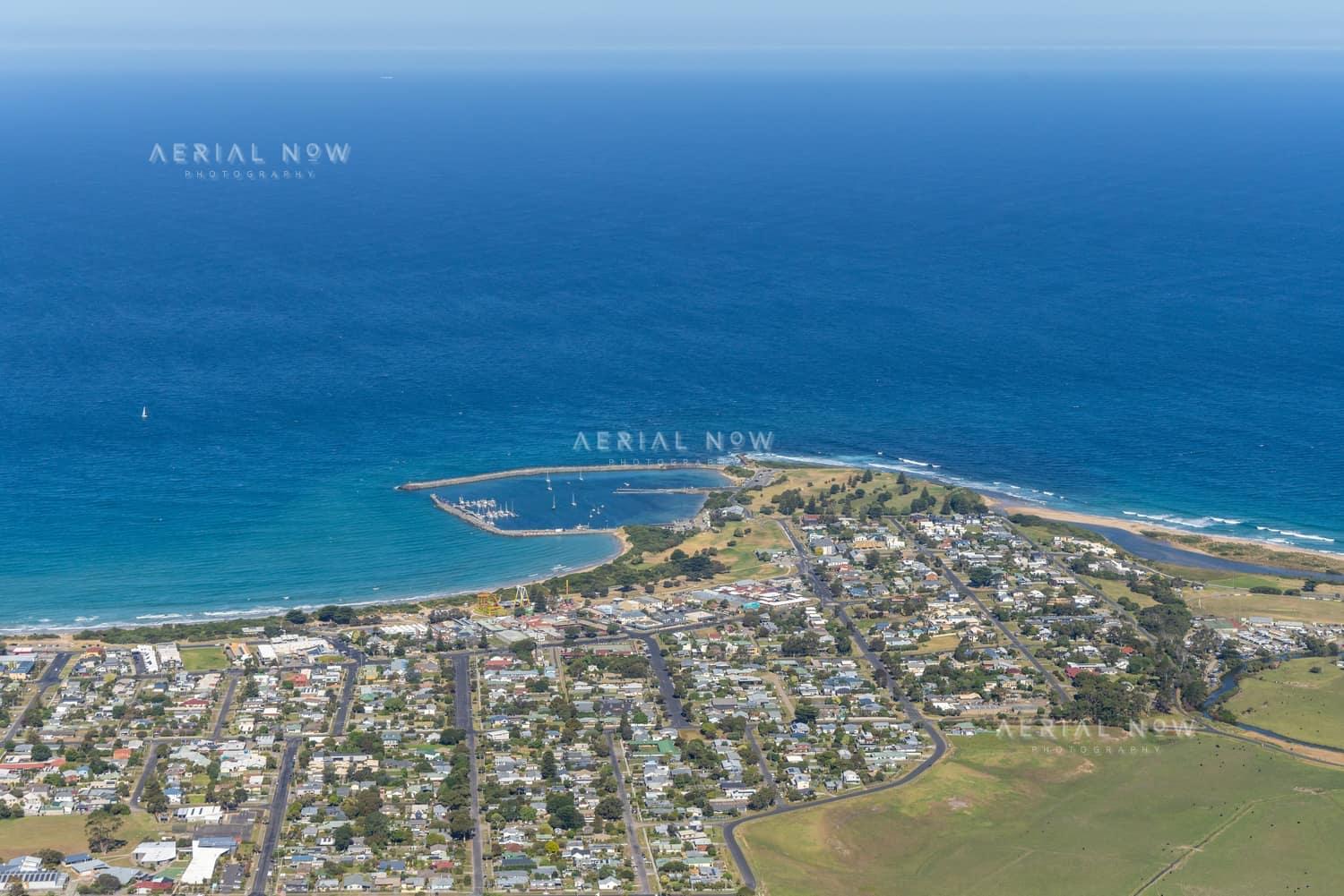 Aerial view of Apollo Bay Harbour, the coastal township, beaches, residential streets and farmland beside the Southern Ocean in Apollo Bay, Victoria.