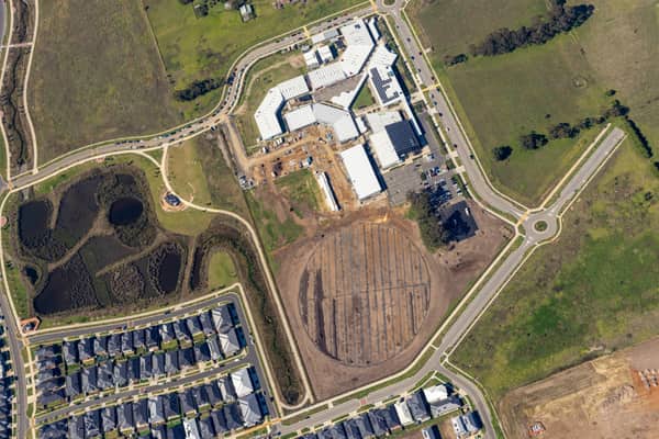 Aerial view of Clyde Secondary College on Woodfield Avenue in Clyde, showing campus buildings, hardcourts, car parking, earthworks and a prepared sports oval area beside nearby residential streets.